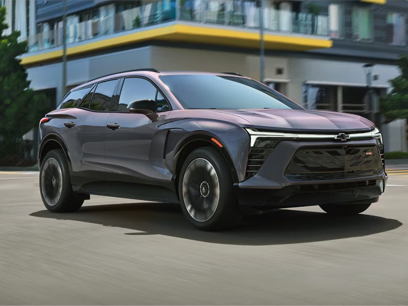 Sleek gray SUV driving on urban street, with modern buildings in the background.