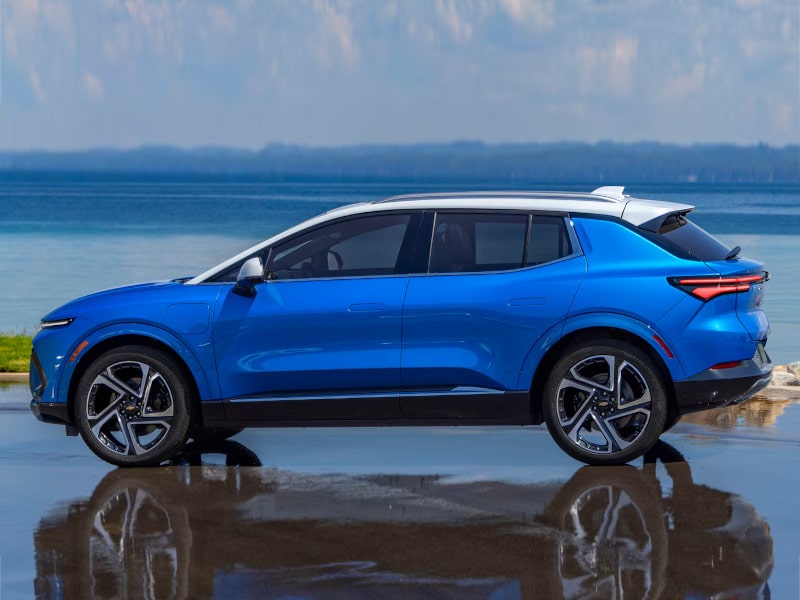 Blue SUV parked by a lake with calm water and a clear sky in the background.