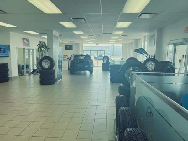 Car showroom interior with parked vehicle, stacks of tires, and bright overhead lighting.