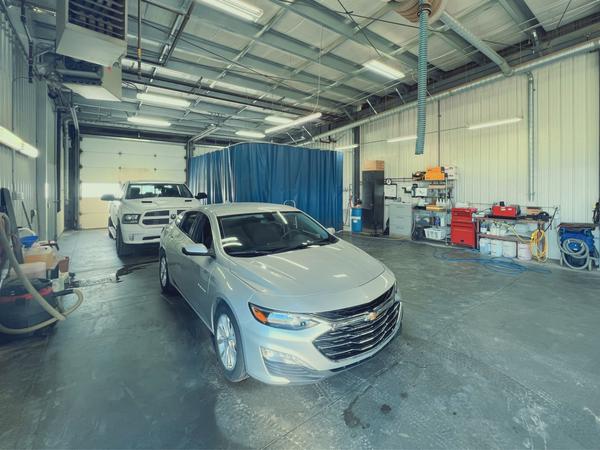 Silver car parked in a spacious garage with tools and equipment along the walls.