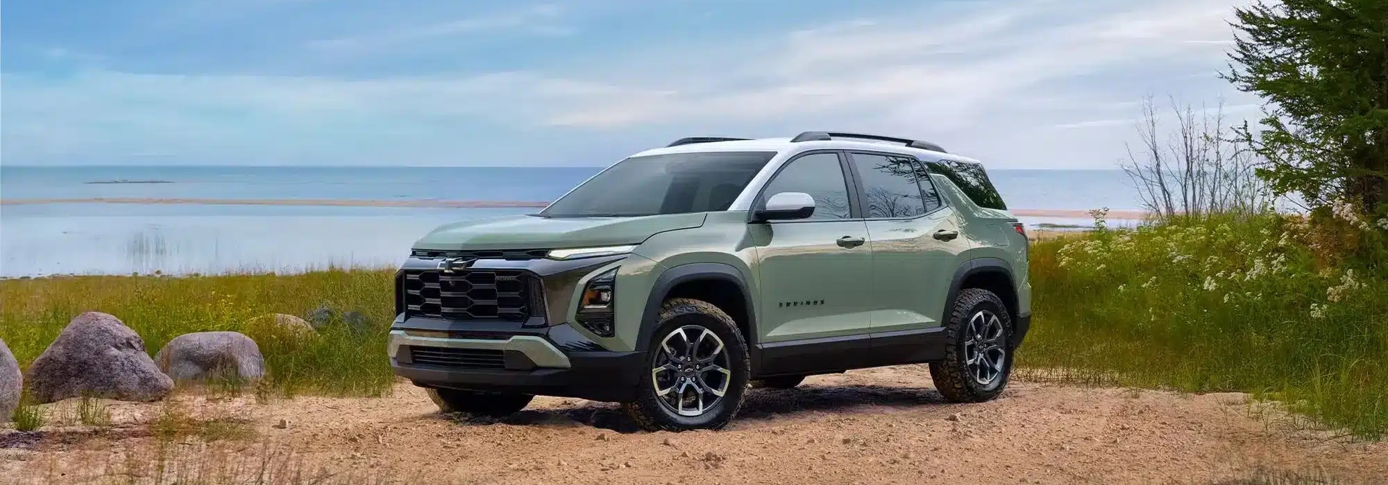 SUV parked by a scenic lakeside with greenery and rocks, under a clear blue sky.