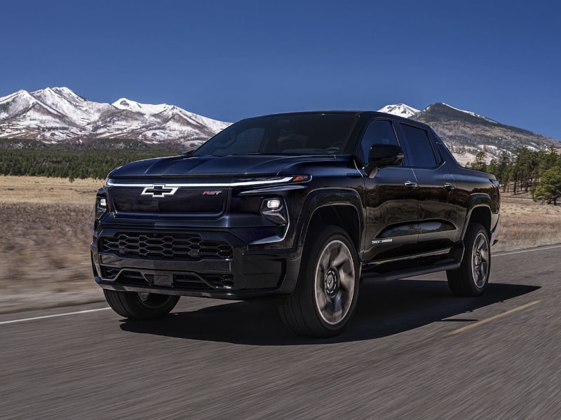 Black Chevrolet pickup truck driving on highway with snowy mountains in background.