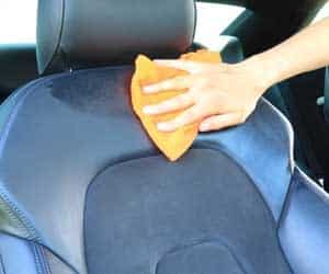 Hand cleaning a black car seat with an orange cloth, focusing on upholstery maintenance.