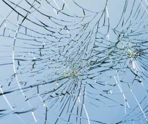 Close-up of cracked glass with intricate spiderweb-like patterns against a light blue background.