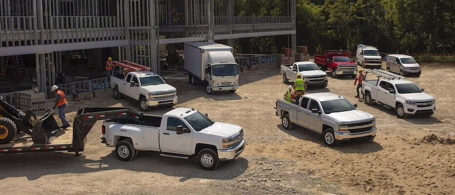 Several white trucks and workers on a construction site near a building frame.