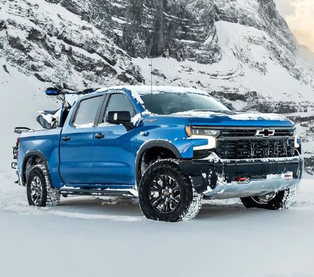 Blue truck parked on snowy terrain with mountainous backdrop, showcasing rugged capability.