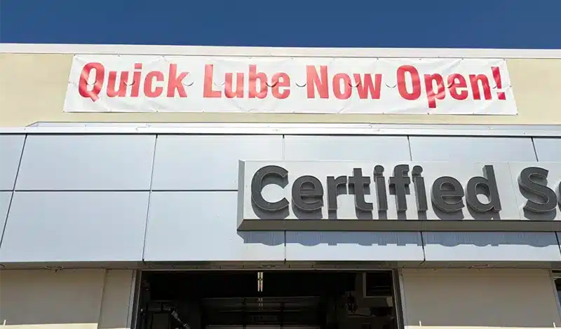 Banner on building reading "Quick Lube Now Open!" against a blue sky.