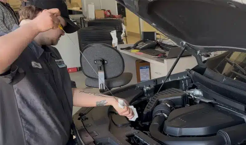 Mechanic checking oil level under the hood of a car in an auto repair shop.